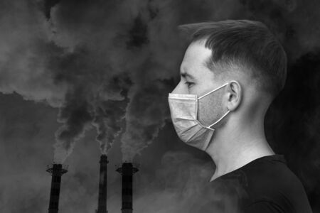 Double exposure portrait of an adult man in a protective mask and industrial exhaust pipes with smoke. Air pollution concept. Black and white image, copy space and horizontal orientation.の写真素材