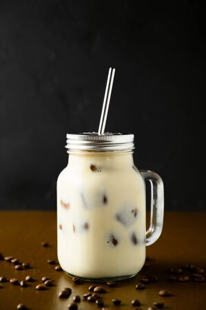 Iced coffee in a glass jar with a metal straw on a brown table, dark backdrop. Vertical orientation, copy space.の写真素材