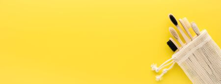 Zero waste concept. Set of eco natural bamboo toothbrushes in a cotton bag on a bright yellow background. Top view, copy space, extra wide banner. Eco-friendly, no plastic.の写真素材