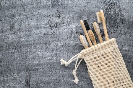 Zero waste concept. Set of eco natural bamboo toothbrushes in a cotton bag on a gray wooden background. Top view, copy space, horizontal orientation. Eco-friendly, no plastic.の写真素材