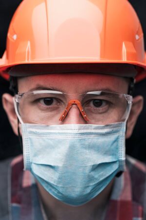Close-up portrait of a worker in a helmet, mask and safety glasses. Vertical orientation.の写真素材