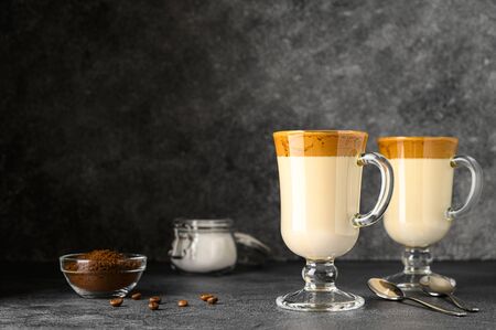 Korean Dalgona coffee in tall glass mugs. Trendy refreshment creamy whipped iced coffee. Horizontal orientation, copy space. Dark background.の写真素材