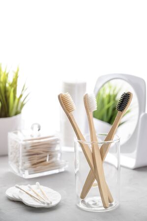 Without plastic concept. Eco friendly bathroom accessories. Bamboo toothbrushes, cotton pads and cotton buds on a light gray table. Zero waste. Copy space, vertical orientation.の写真素材