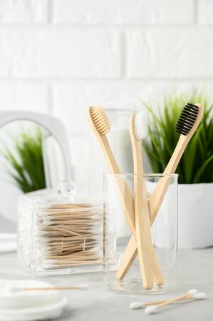 Without plastic concept. Eco friendly bathroom accessories. Bamboo toothbrushes, cotton pads and cotton buds on a light gray table. Zero waste. Copy space, vertical orientation.の写真素材