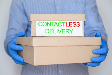 Safe, contactless delivery to home during coronavirus pandemic. Courier in a blue shirt and medical glove holds cardboard boxes. Stay home.の写真素材