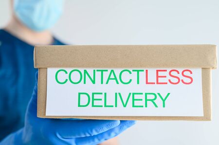 Safe, contactless delivery parcels to home. Courier in a blue glove holds a cardboard box on a light background. Stay home. Horizontal orientationの写真素材