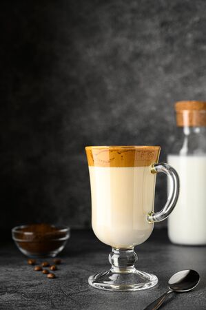 Iced Dalgona coffee in glass mug on dark background. Trendy refreshment creamy whipped iced coffee. Korean coffee drink. Vertical orientation, copy spaceの写真素材
