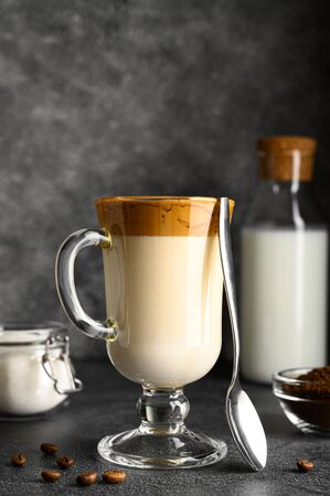 Closeup of Iced Dalgona coffee in glass mug and teaspoon on dark background. Trendy refreshment creamy whipped iced coffee. Korean coffee drink. Copy spaceの写真素材