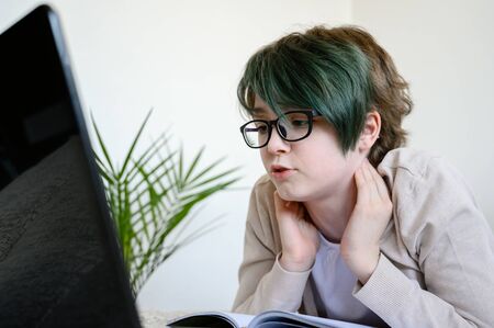 Distance learning online education. Teen schoolgirl studying at home, using laptop. Caucasian girl with glasses lies on bed and doing school homework. horizontal shot.の写真素材