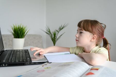 Distance learning online education. Schoolgirl studying at home, using laptop. Caucasian kid sits by the table and doing school homework. Copy space, horizontal shot.の写真素材