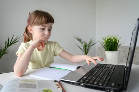 Distance learning online education. Schoolgirl studying at home, using laptop. Caucasian kid sits by the table and doing school homework. Copy space, horizontal orientation.の写真素材