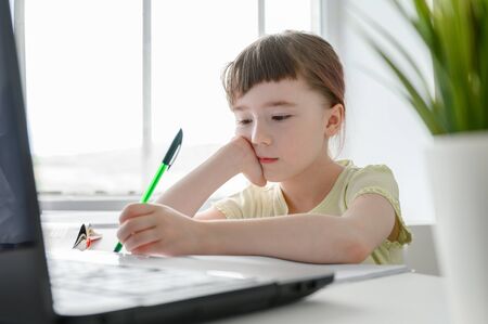 Distance learning online education. Schoolgirl studying at home, using laptop. Caucasian kid sits by the table and doing school homework. horizontal shot.の写真素材