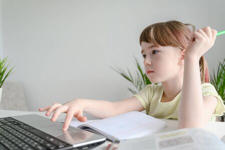 Distance learning online education. Schoolgirl studying at home, using laptop. Caucasian kid sits by the table and doing school homework. Copy space, horizontal.の写真素材