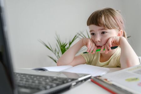 Distance learning online education. Schoolgirl studying at home, using laptop. Caucasian kid sits by the table and doing school homework. Copy space, horizontal shot.の写真素材