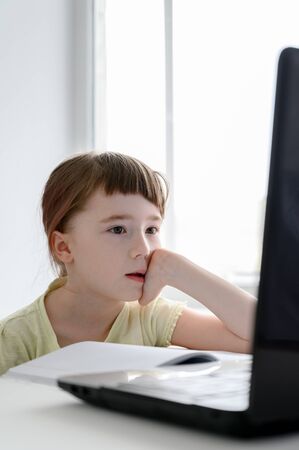 Distance learning online education. Teen schoolgirl studying at home, using laptop. Caucasian girl sits by the table and doing school homework. Copy space, vertical shot.の写真素材