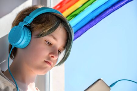 Sad teenage girl in headphones listening to music, leaning on the window. Misses her friends. Quarantine self-isolation.の写真素材