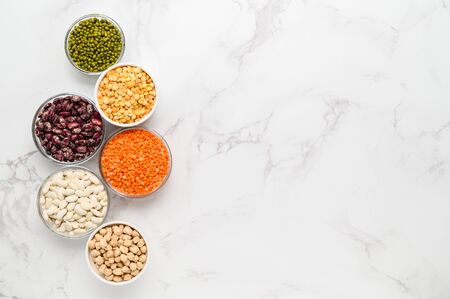 Various sources of vegetable protein: beans, lentils, peas, chickpeas, mung bean in bowls. A healthy balanced diet for vegans and vegetarians. Light marble background. Flat lay, copy space.の写真素材