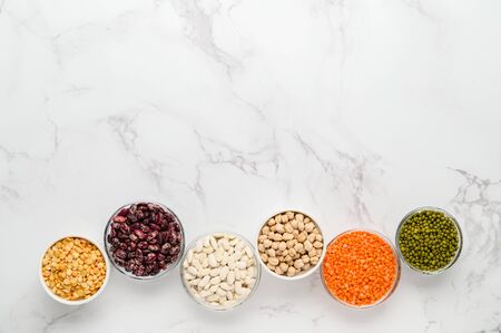 Various sources of vegetable protein: beans, lentils, peas, chickpeas, mung bean in bowls. A healthy balanced diet for vegans and vegetarians. Light marble background. Top view, copy space.の写真素材