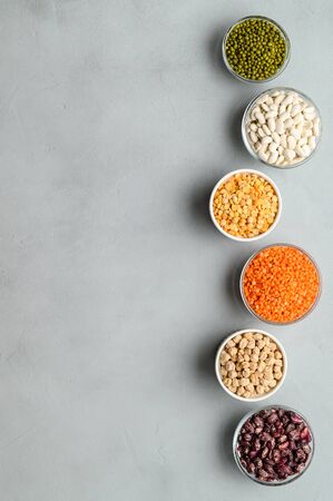 Sources of vegetable protein. Different types of legumes in bowls on gray stone background. Vegan and vegetarian food concept. Flat lay, vertical orientation, copy space.の写真素材