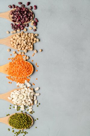 Sources of vegetable protein. Different types of legumes in wooden spoons on gray stone table. Vegan and vegetarian food concept. Flat lay, copy space.の写真素材