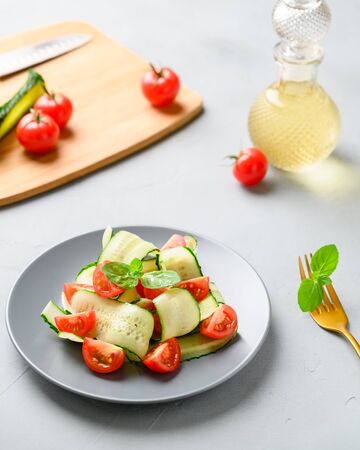 Healthy vegetable salad of fresh cherry tomatoes, cucumbers on a plate. Vegan food. Summer refreshing detox salad. Light gray stone table. Vertical orientation.の写真素材