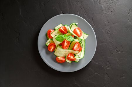 Healthy vegetable salad of fresh cherry tomatoes, cucumbers on a plate. Vegan food. Summer refreshing detox salad. Dark stone table. Top view, copy spaceの写真素材