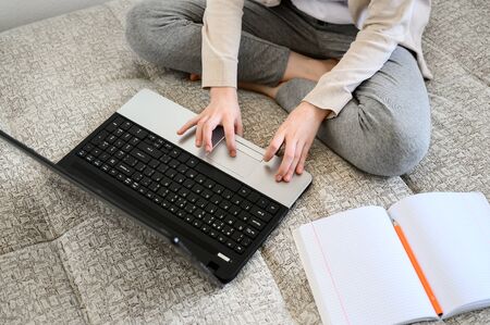 Distance learning online education. Teen schoolgirl studying at home, using laptop. Girl sitting on bed and doing school homework. horizontal orientation.の写真素材