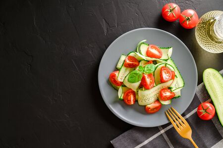 Healthy vegetable salad of fresh cherry tomatoes, cucumbers on a plate. Vegan food. Summer refreshing detox salad. Dark stone table. Top view, copy spaceの写真素材
