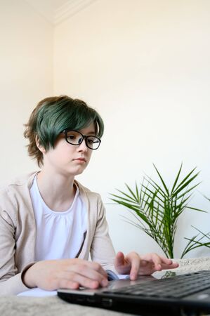 Distance learning online education. Teen schoolgirl studying at home, using laptop. Caucasian girl with glasses lies on bed and doing school homework. Copy space, vertical orientation.の写真素材