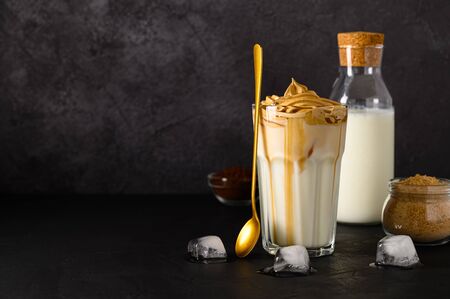 Closeup of Iced Dalgona coffee in glass mug and teaspoon on dark background. Trendy refreshment creamy whipped iced coffee. Korean coffee drink. Copy spaceの写真素材