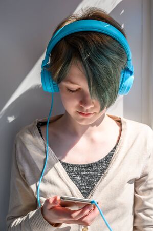 Sad teenage girl in headphones listening to music, leaning on the window. Misses her friends. Quarantine self-isolation.の写真素材