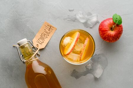 Homemade fermented kombucha in a bottle and in a glass with apples on a light gray stone background. Healthy probiotic apple cider with ice. Top view.の写真素材