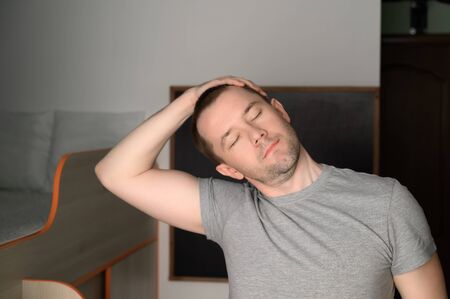 Young adult man doing stretching during a workout at home. Mental health. Home interior, daylight.の写真素材