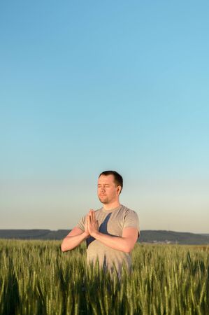 Adult man stands on a field in tall grass doing yoga during sunset. Digital detox, connection with nature concept. Copy space, vertical.の写真素材