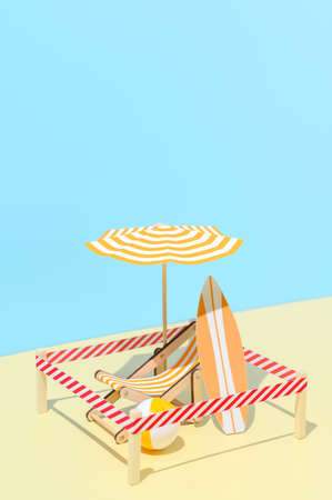 Sunbed with umbrella, surfboard and ball on the beach. Isolated vacation spot at resort. Minimalistic miniature composition. New normal, safe social distance. Copy space.の写真素材