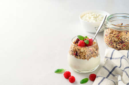 Parfait yogurt with granola and raspberries in a glass, light background, copy space. Healthy breakfast concept.の写真素材