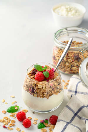 Parfait yogurt with granola and raspberries in a glass, light background, copy space. Healthy breakfast concept.の写真素材