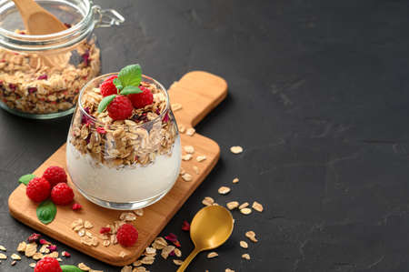 Parfait yogurt with granola and raspberries in a glass, black background, copy space. Healthy breakfast concept.の写真素材