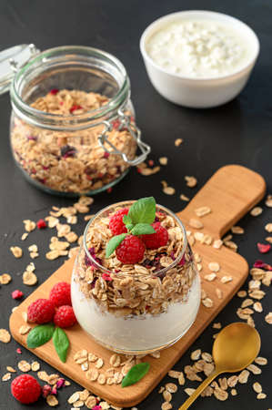 Parfait yogurt with granola and raspberries in a glass, black background, vertical orientation. Healthy breakfast concept.の写真素材
