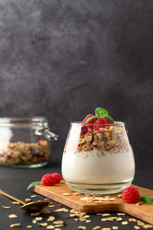 Parfait yogurt with granola and raspberries in a glass, black background, copy space. Healthy breakfast concept.の写真素材