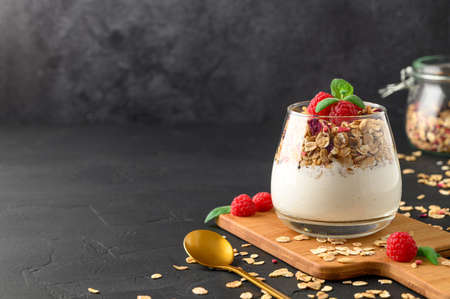 Parfait yogurt with granola and raspberries in a glass, black background, copy space. Healthy breakfast concept.の写真素材