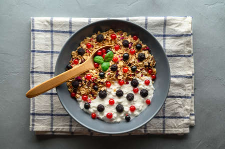 Healthy breakfast. Bowl with oat granola, yogurt and black raspberries, black and red currants on a gray concrete background. Top view.の写真素材