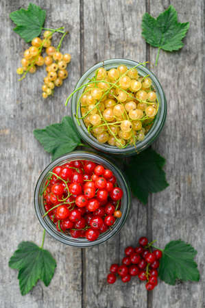 Red and white currants in glass jars. Eco food concept. Top view, vertical orientation.の写真素材
