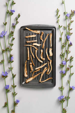Healthly food. Dried chicory roots on a baking sheet. Light gray concrete background. Top view, vertical orientation.の写真素材