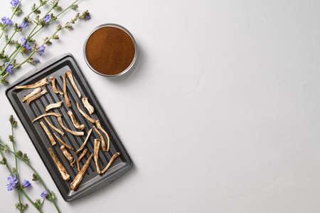 Healthly food. Dried chicory roots on a baking sheet and dry powder in a bowl. A healthy alternative to coffee. Light gray concrete background. Top view, copy space.の写真素材