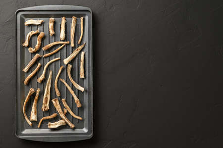 A healthy drink, an alternative to coffee. Dried chicory roots on a baking sheet. Dark concrete background. Top view, space for text.の写真素材