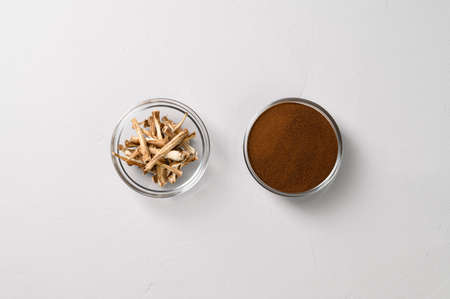 A healthy drink, an alternative to coffee. Dried roots and dry chicory powder in two glass bowls. Light gray concrete background. Top view, space for text.の写真素材