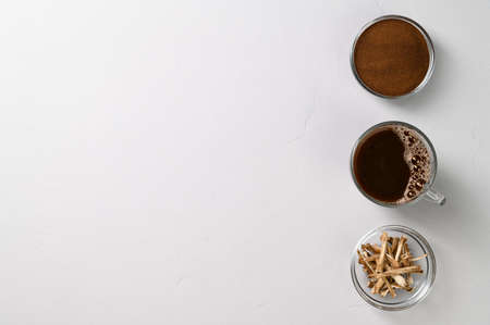 A healthy drink, an alternative to coffee. Chicory drink in a glass cup, dried roots and powder in bowls on a light gray stone background. Top view, space for text.の写真素材
