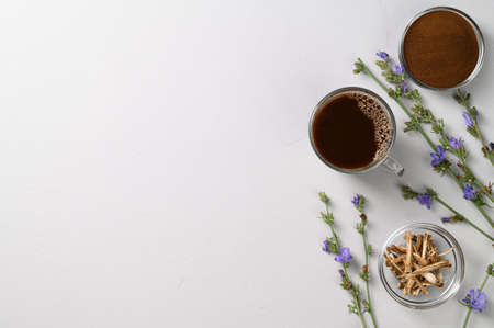 A healthy drink, an alternative to coffee. Chicory drink in a glass cup, dried roots and powder in bowls on a light gray stone background. Top view, space for text.の写真素材