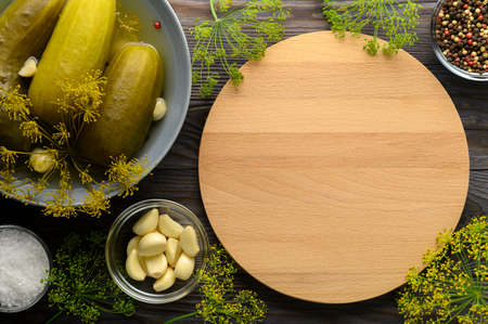 Healthy fermented vegan food. Empty cutting board, fermented cucumbers in a plate and spices on a wooden background. Top view, copy space.の写真素材